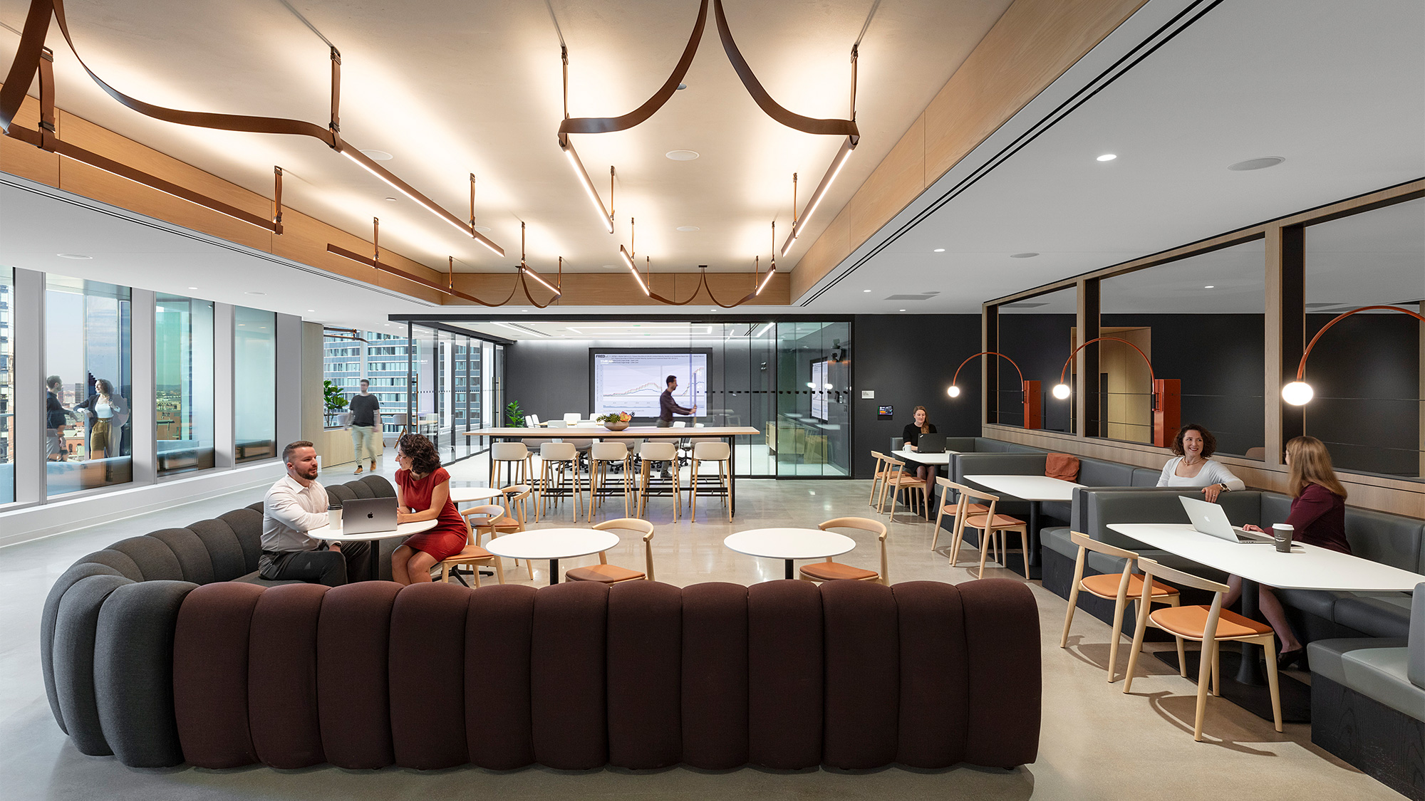 A group of people sitting at a table in a room with a large screen.
