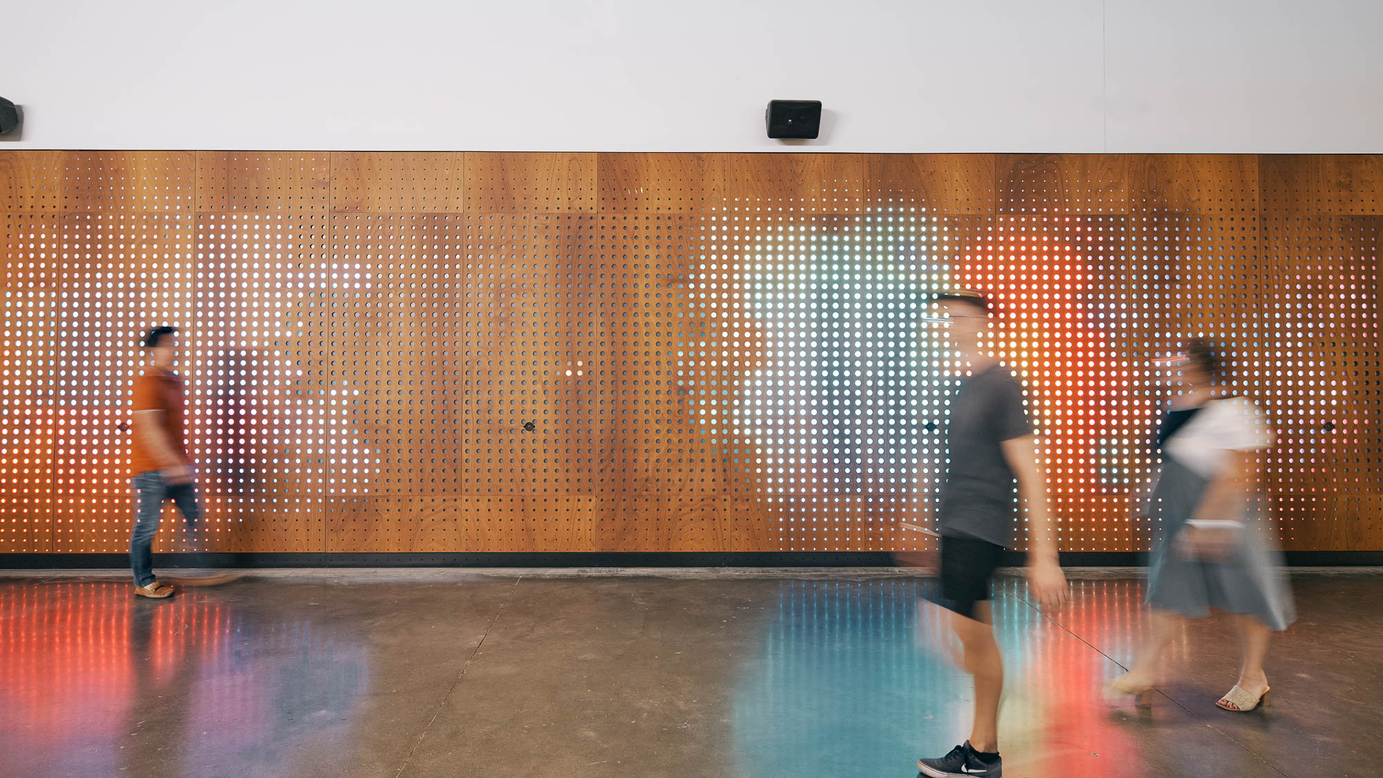 A group of people walking in a room with a wall of lights.