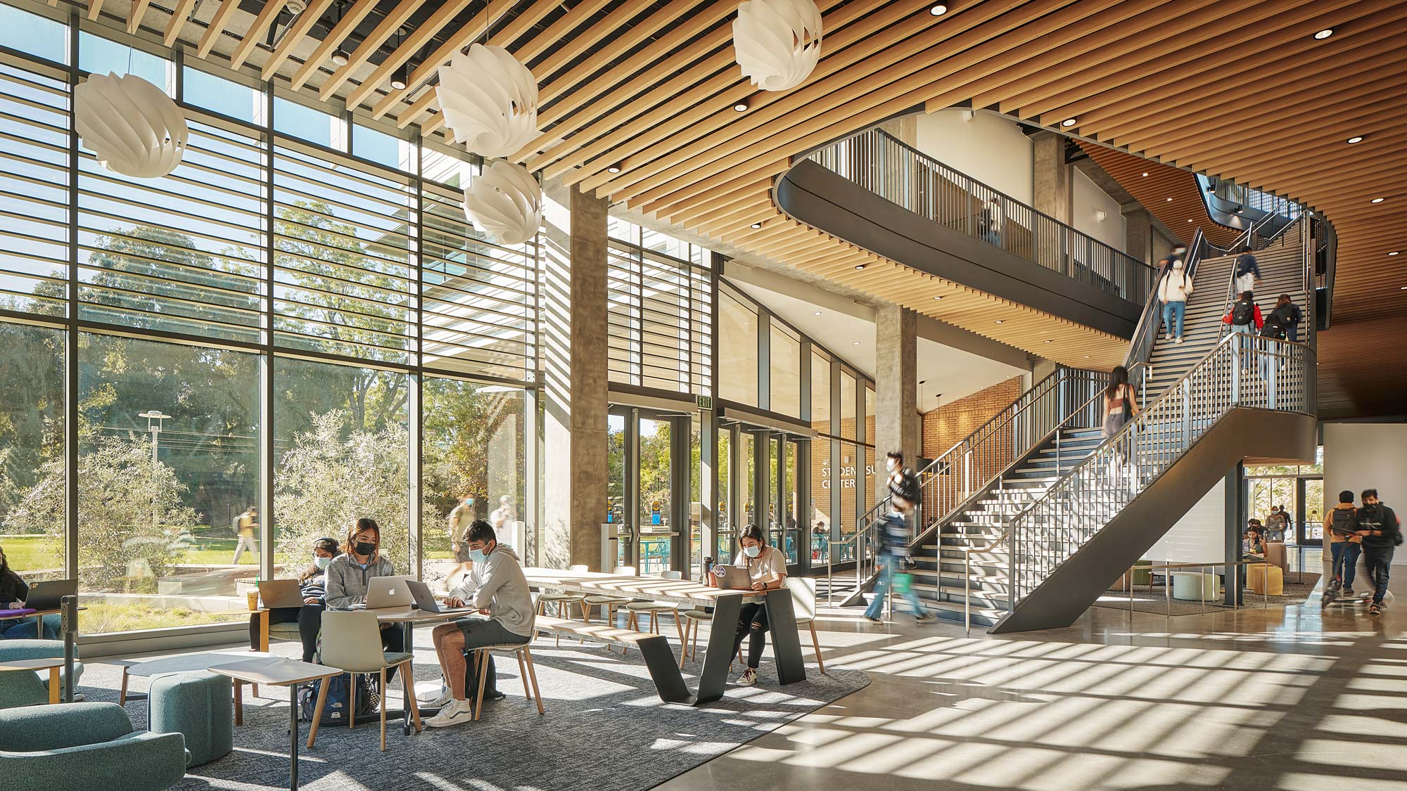 A group of people sitting at tables in a large room with large windows.